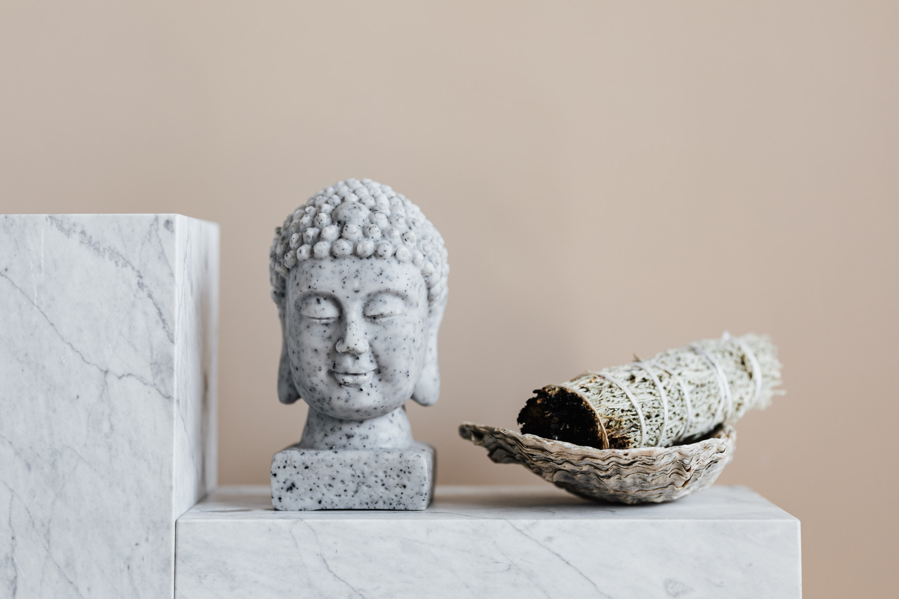 Small stone buddha and sage incense bundle in bowl on marble shelf